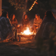 Group of women sitting quietly around a glowing campfire in nature, wrapped in blankets, sharing warmth and stillness under the evening sky.